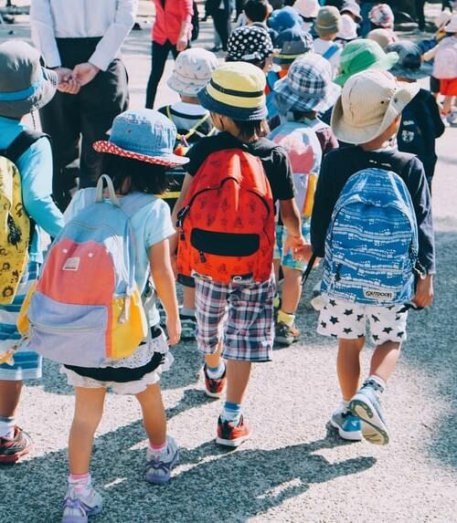 dzieci z plecakami na wycieczce szkolnej, idące razem trzymając się za ręce